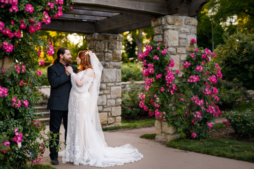 Photograph of a bride and a groom surrounded by rose arches